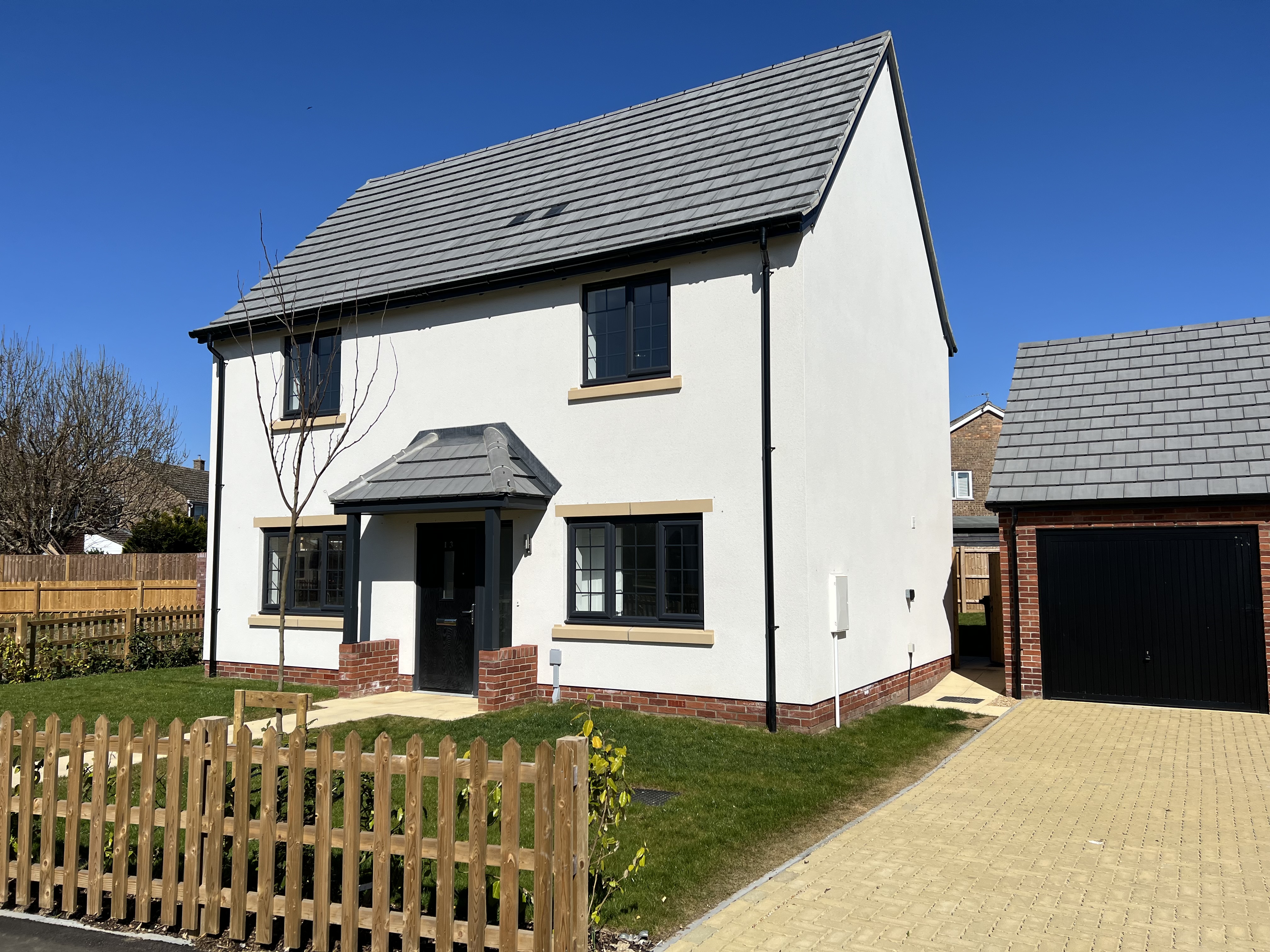 Two storey white house with a paved driveway and garden with a fence in front