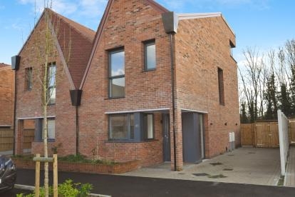 A semi-detached property with red brickwork and a quirky slanted roof. The two-storey house has driveway parking, and features dark window and door frames