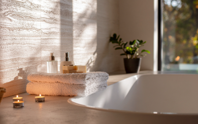 A warm relaxing photo of bath with lit candles, towels and skincare products on the side of it.